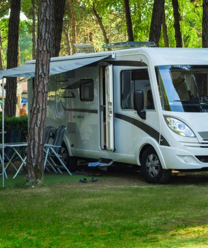 Camper bianco parcheggiato in un campeggio tra gli alberi.