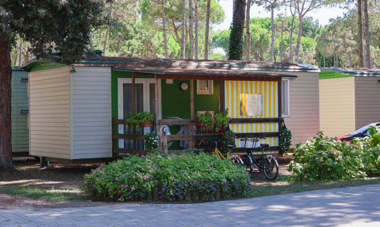 Mobile home with a porch and bikes, surrounded by greenery.