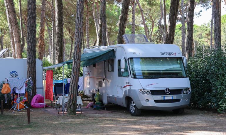 Campingvogn på campingplads blandt træer, med telte og stole.