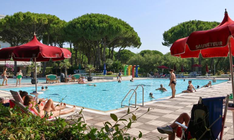 Piscina all'aperto con ombrelloni rossi e persone che si rilassano.