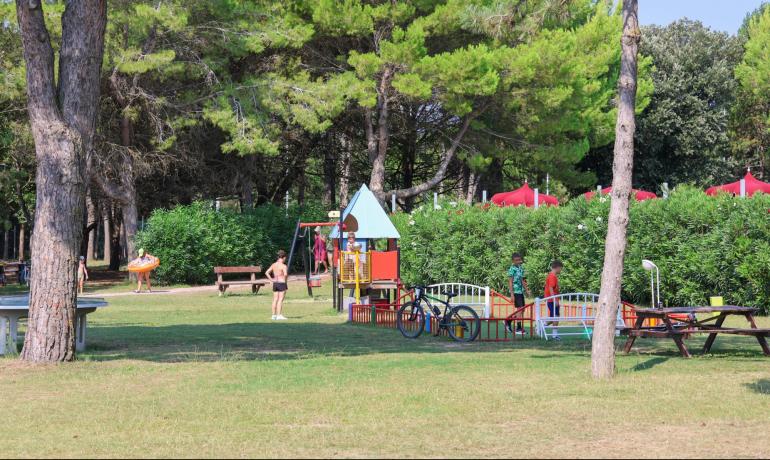 Parco giochi all'aperto con bambini e alberi verdi.