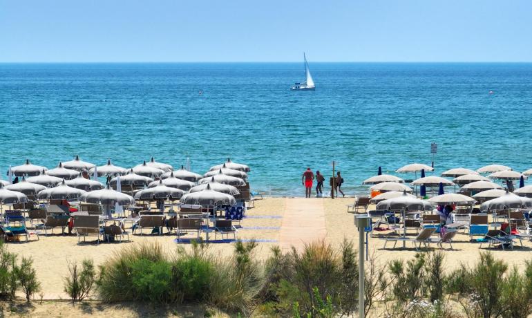 Spiaggia sabbiosa con ombrelloni e barca a vela sul mare.