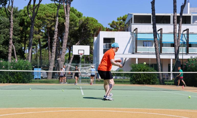 Tennisspillere på en udendørs bane med træer og bygning i baggrunden.